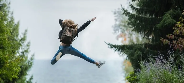 Excited girl with a backpack mid-jump.