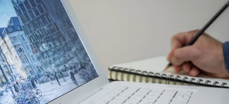 A person's hand writing down things from the laptop.