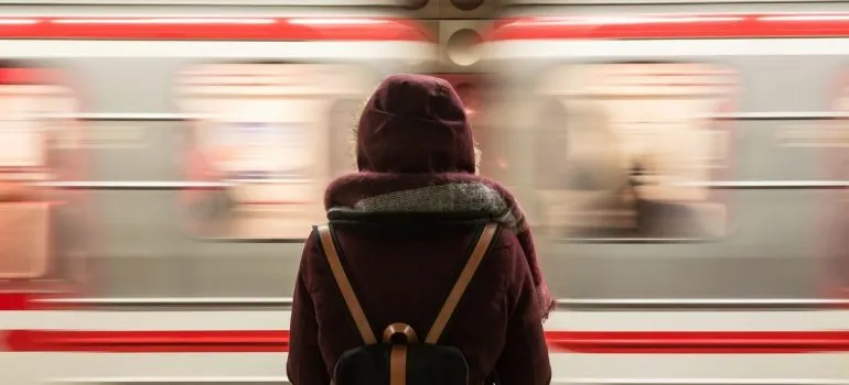 a woman wearing a jacket standing near a passing train