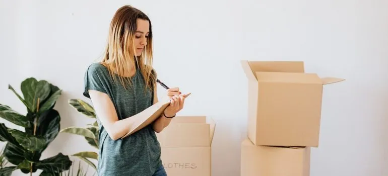 a woman writing a list while standing next to cardboard boxes