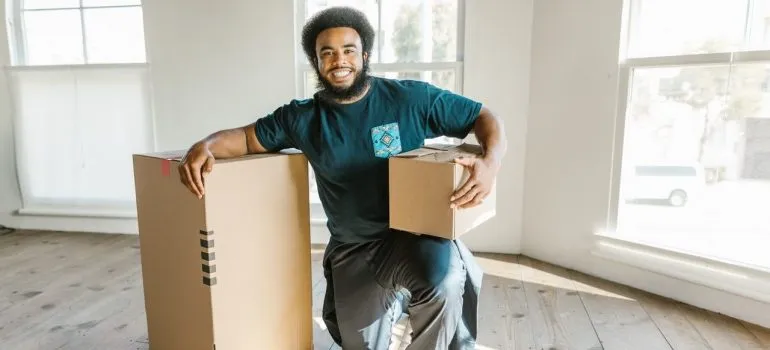 a man working for a moving company kneeling next to cardboard boxes