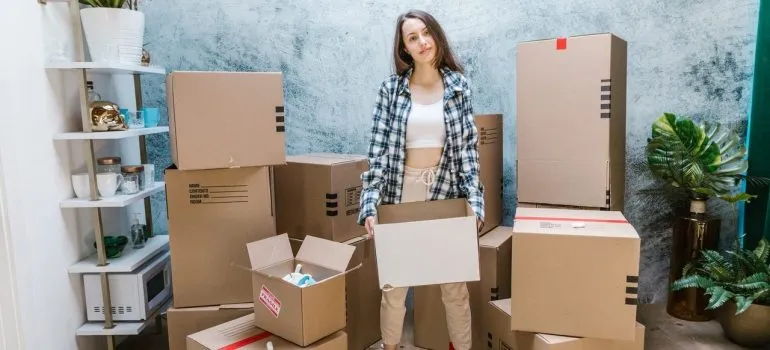 a woman holding a cardboard box while standing between a pile of them