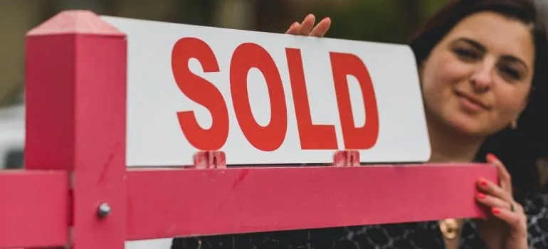 a woman putting a "sold" sign after purchasing a home