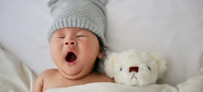 an infant yawning in its nursery with a toy beside it