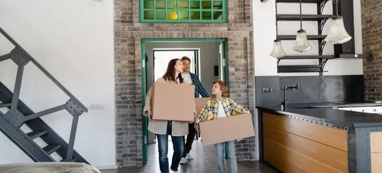 a family of three walking with boxes as they organize a family move to Olney