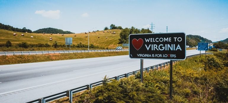 a sign that says welcome to virginia at the side of the road with a farm behind it