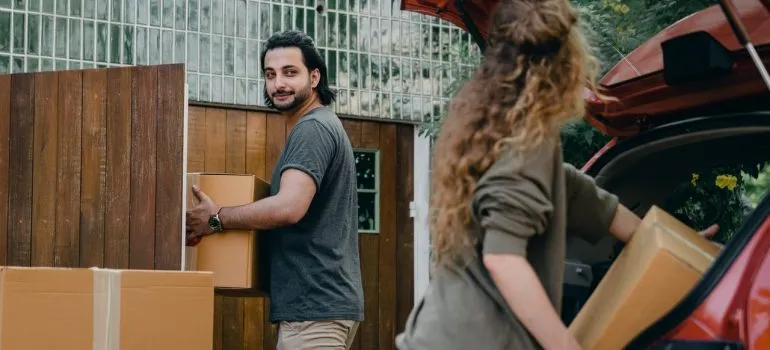 a couple packing cardboard boxes in the car thelsemves after they found cheap ways to move cross country