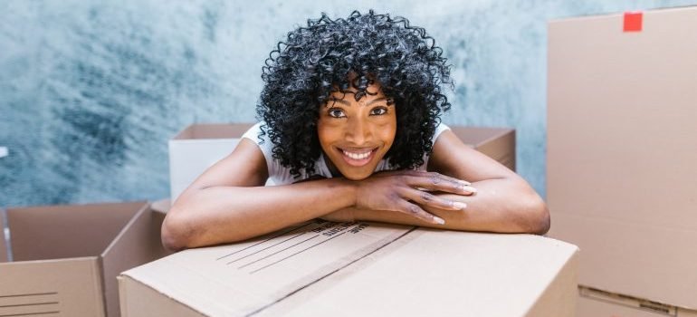 A woman with hands on a box smiling.
