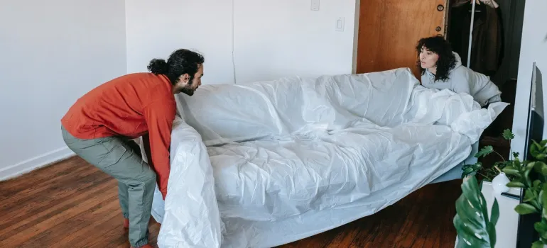 a couple handling a larger couch in their living room