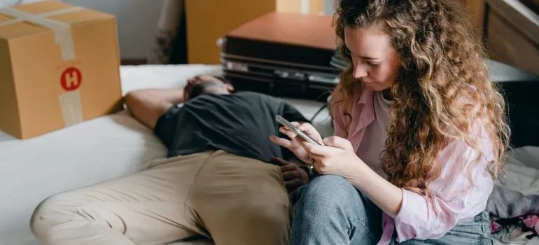 A couple being idle in the midst of packing a bedroom.