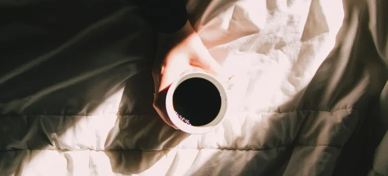 a person holding a cup of coffee on the ray of morning sunshine on their bed