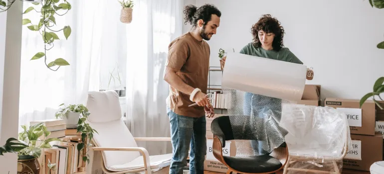 a happy couple handling bubble wrap while trying to pack a chair as one of the main reasons to hire professioanls when moving locally in Maryland