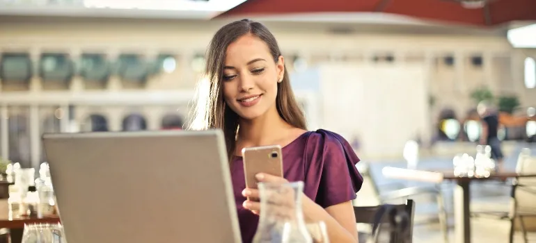 woman sitting and working on her laptop while holding phone