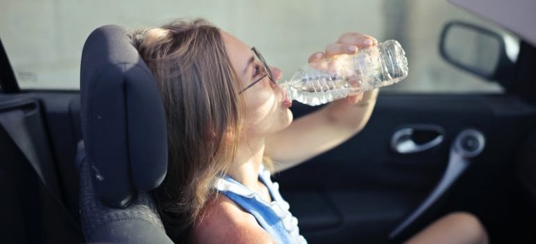 Girl drinking water in the car, hydrating is important to survive long distance relocation n summer