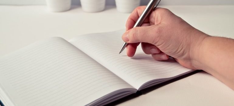 a person holding a pen and writing in a white notebook about how to move on budget in DMV