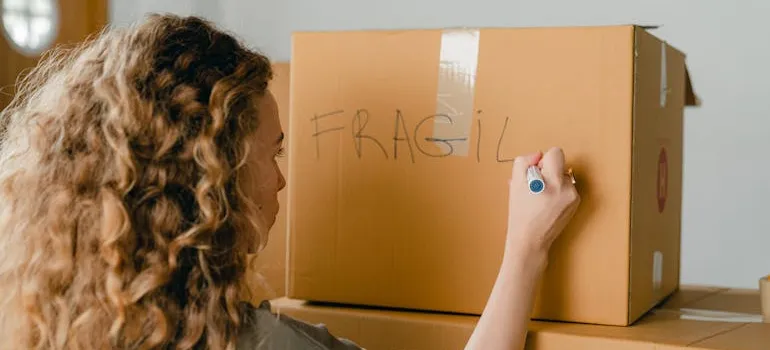 A woman labeling a cardboard box before cross country moving.