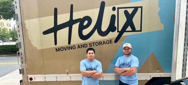 Professional movers standing next to a moving van and ready to help you relocate to one of the best places according to Maryland moving trends.