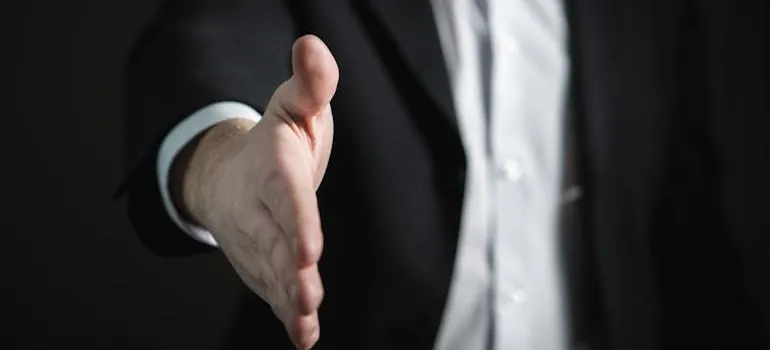 A man in a suit offering a hand for a handshake.
