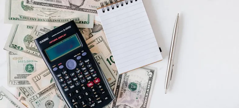A calculator, a pile of cash, a notebook, and a pen.
