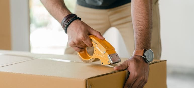 A person taping a cardboard moving box after learning all about Gaithersburg relocation mistakes to avoid.